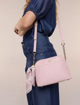 Cartera bandolera estructurada de eco cuero rosado con textura graneada, silueta curva y cierre superior. Posee correa larga regulable con detalles de cadena dorada, bolsillo frontal con logo metálico, pañuelo estampado a contratono anudado en un lateral y base rígida con apoyos metálicos.