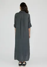 Vestido camisero largo de lino, color mostaza, con cuello camisero, cierre frontal de botones y mangas tres cuartos con detalle de tejido calado en los laterales.