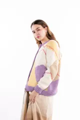 Cárdigan de punto con diseño de rombos en tonos crema, amarillo, beige y lila. Presenta cierre frontal con botones, cuello redondo y puños acanalados en color lila.