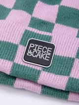 Gorro de tejido de punto con diseño a cuadros en color naranja y beige, con un parche negro con la inscripción "PIECE OF CAKE" en blanco.