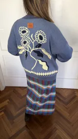 Saco tipo cardigan de punto jacquard color azul, con cierre frontal de aluminio. Presenta un diseño floral en la espalda y detalle de rombos en el ruedo y puños.