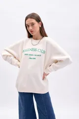 Buzo de algodón color crudo con cuello redondo y manga larga. Presenta bordado frontal en color verde que dice "Wellness Club Body. Mind. Balance Since 1994".