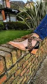 Zapatos de cuero color tostado con puntera fina y taco bloque de madera de 6 cm. Cuentan con tiras cruzadas con estampado animal print de leopardo en el empeine, talón negro y tira al tobillo con hebilla metálica ajustable.