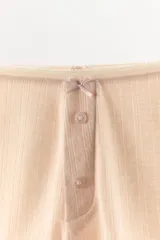 Shorts de estilo culotte confeccionados en tejido pointelle, con tiro alto y cintura elástica. Presentan una abertura frontal decorativa con botones a tono y un pequeño lazo decorativo en la cintura.