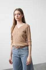 Remera de manga larga color beige, confeccionada en algodón, con escote en V y cartera corta de botones blancos.