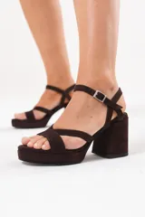 Sandalias de gamuza color chocolate, con plataforma, taco ancho y tiras cruzadas en la parte delantera. Cuentan con tira ajustable con hebilla en el tobillo.