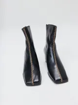 Botas de cuero negro con punta cuadrada, taco ancho de madera y costura decorativa bordada en contraste a lo largo del empeine. Cuenta con cierre en la parte trasera.