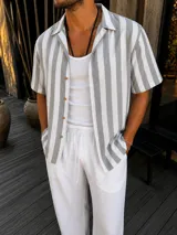Camisa de manga corta con diseño a rayas verticales en color gris y blanco, cuello camisero y cierre frontal con botones.