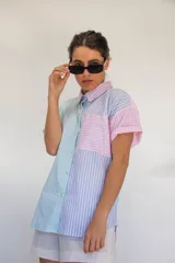 Camisa de manga corta con diseño de rayas en tonos rosa, celeste, verde y blanco. Cuenta con cuello camisero, cierre frontal con botones y un bolsillo en el pecho.