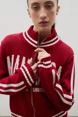 Campera tejida de punto color marrón con cierre frontal completo, cuello alto y detalles de rayas blancas en cuello, puños y ruedo. Presenta el logo de la marca estampado en el frente.