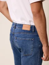 Pantalón de jean corte recto en color azul medio, con cierre de botón y cremallera, y bolsillos laterales y traseros.