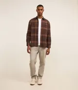 Camisa de manga larga con diseño de cuadros en tonos marrones, confeccionada en algodón. Presenta cuello camisero, cierre frontal con botones y un bolsillo en el pecho con botón.