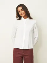Camisa de manga larga color blanco, con cuello alto tipo mao con detalle de volados y cierre frontal de botones.