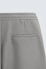 Bermuda negra de corte recto, con cintura elástica ajustable mediante cordón, pliegues frontales y bolsillos de vivo en la espalda. El bajo tiene un dobladillo vuelto.