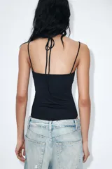 Body negro de tejido elástico con escote redondo y tirantes finos. Presenta un panel superior de encaje floral a tono con diseño halter ajustable mediante lazada en el cuello y cierre inferior con botones a presión.