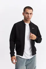 Campera tipo bomber color negro con cierre frontal completo, cuello redondo acanalado y puños elásticos. Presenta una textura sutil en la tela y un pequeño logo bordado en el pecho.