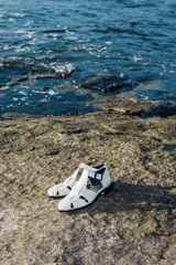 Sandalia cerrada tipo pescador, color blanco o hueso brillante, con tiras entrecruzadas en el empeine y cierre de hebilla ajustable en el lateral. Posee suela y taco bajo de color negro.