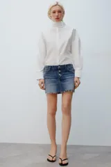 Camisa amplia blanca de cuello alto y manga larga, con cierre frontal de botones.