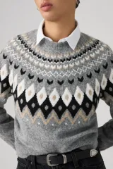 Sweater de punto con diseño Fairisle en el canesú, cuello redondo, manga larga y puños acanalados. Presenta un patrón geométrico en tonos gris, negro, blanco y beige sobre una base gris jaspeado.