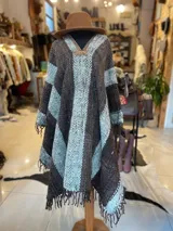 Poncho de lana virgen tejido en telar con diseño geométrico a rayas en tonos gris, marrón y celeste, con apliques de cuero en el escote y flecos en el ruedo.