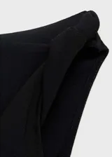 Top sin mangas de color negro con cuello asimétrico y detalle drapeado en la parte superior. Presenta un diseño recto y cierre de cremallera lateral.