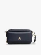 Cartera tipo cámara estructurada de color azul marino, con solapa frontal y logo metálico de Tommy Hilfiger en dorado. Posee un bolsillo externo con cierre de solapa a broche y correa ajustable extraíble.