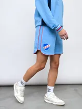 Short de felpa celeste, de corte deportivo, con detalles de pipings tricolor en los bordes y escudo del Club Nacional de Football aplicado en la pierna.