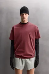 Camiseta de entrenamiento de ajuste relajado, color vino tinto, confeccionada en tejido de peso medio con mezcla de algodón. Presenta cuello redondo con acabado en vivo doble y manga corta.