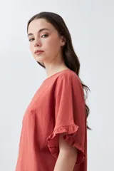 Blusa blanca de corte holgado con cuello redondo, mangas cortas con detalle de volados y ruedo con terminación de volado pequeño.