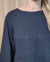 Remera de manga larga color blanco, con cuello redondo y dos bolsillos frontales tipo parche. Presenta un corte recto y holgado con un diseño minimalista.