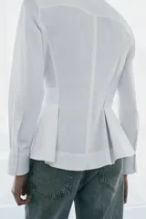 Camisa de popelín de algodón con cuello solapa, manga larga con puños y bajo con diseño peplum. Presenta cierre frontal oculto con botones.