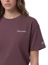 Remera de corte boxy y cuello redondo, confeccionada en algodón color violeta. Presenta un gráfico bordado con el logo de la marca en el pecho y un parche tejido distintivo en la manga.