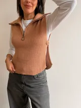 Chaleco de tejido de punto acanalado en color camel, con cuello polo, medio cierre frontal y aberturas laterales con detalle de botones.