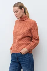Polera de tejido de punto color ocre con cuello alto, diseño de rombos en relieve en el frente y mangas con detalle de trenzas laterales.