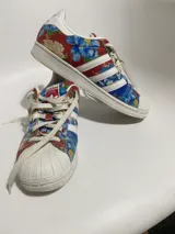 Championes Adidas modelo Superstar, con diseño estampado floral en tonos azules, rojos y amarillos sobre base de tela, con la clásica puntera de goma blanca y cordones blancos.