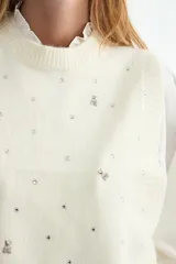 Chaleco de punto color crema con cuello redondo, decorado con pequeños apliques brillantes distribuidos por toda la prenda.