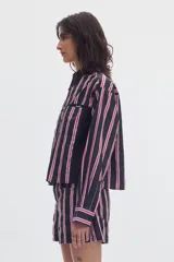 Camisa cropped de manga larga negra con estampado de lunares blancos, cuello camisero, cierre frontal de botones y bolsillos plaqué en el pecho.