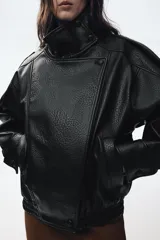 Cazadora de efecto piel con cuello subido, manga larga con puños, trabillas en los hombros y bolsillos laterales. Cuenta con cierre frontal de cremallera y solapa con botones a presión.