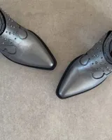 Botines cortos plateados de cuero vacuno, con punta fina, taco bajo y detalle de tachas y correas alrededor del tobillo.