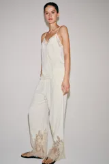 Pantalón de tiro medio con cintura elástica ajustable mediante cordones. Presenta un diseño fluido con bolsillos laterales ocultos y bajo decorado con una aplicación de encaje a contraste.