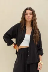 Camisa negra de manga larga, corte oversize, con cierre frontal de botones y cuello camisero.