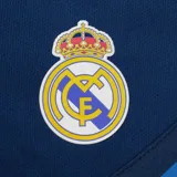 Short de fútbol azul marino con cintura elástica y cordón ajustable. Logo del Real Madrid bordado en la pierna derecha y tres tiras horizontales en el ruedo.