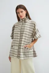 Capa acampanada color beige con manga corta, cierre metálico a la vista, cuello recto, bolsillos con tapa y terminaciones envivadas. Confeccionada en lana fina sin teñir, diseñada exclusivamente por Don Baez.