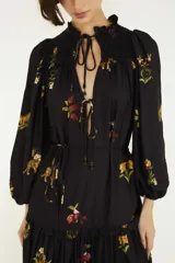 Vestido largo negro de mangas largas con puños elastizados, escote en V con lazo regulable y falda amplia con recorte fruncido, confeccionado en tejido liviano con estampado floral e inspirado en la selva.