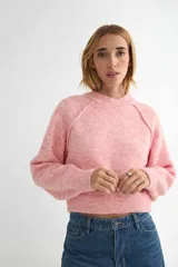 Buzo de tejido de punto con cuello redondo, diseño cropped y mangas largas con puños acanalados. Presenta una textura jaspeada en tono beige.