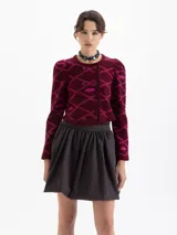 Saco tipo cardigan corto tejido en jacquard con diseño gráfico de labios y cadenas. Presenta cuello redondo, mangas largas con hombros ligeramente abullonados y cierre frontal con botones.