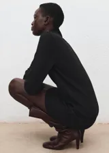 Vestido corto de punto negro con cuello alto y detalle de botones metálicos en el hombro.