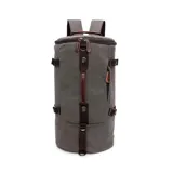 Bolso mochila de lona canvas gris con detalles en marrón, diseño cilíndrico, múltiples asas, correas ajustables y bolsillos con cierre.