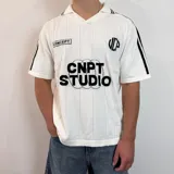 Chomba de punto blanca con cuello tipo polo, mangas cortas con rayas negras en los hombros y logo de la marca en el pecho.