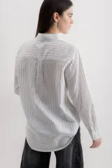 Camisa de corte clásico con cuello camisero, manga larga con puños abotonados y cierre frontal con botones. Presenta un diseño de rayas verticales finas en color negro sobre fondo blanco.